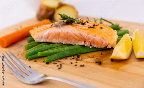 Grilled fresh salmon steak with roasted green beans, baked potatoes, lime and salad vegetables is a healthy diet for dieting on a wooden plate.