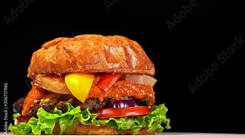 Craft burger is cooking on black background in black food gloves. Consist: red sauce salsa, lettuce, red onion, pickle, cheese, chilli green pepper, air bun and marbled meat beef. Not made ideal photo