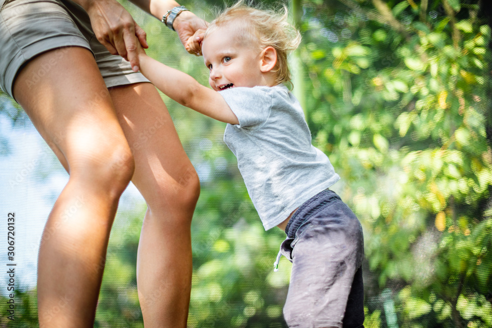 Little child with his mom playing on trampoline outdoor in backyard Little child with his mom playing on trampoline outdoor in backyard