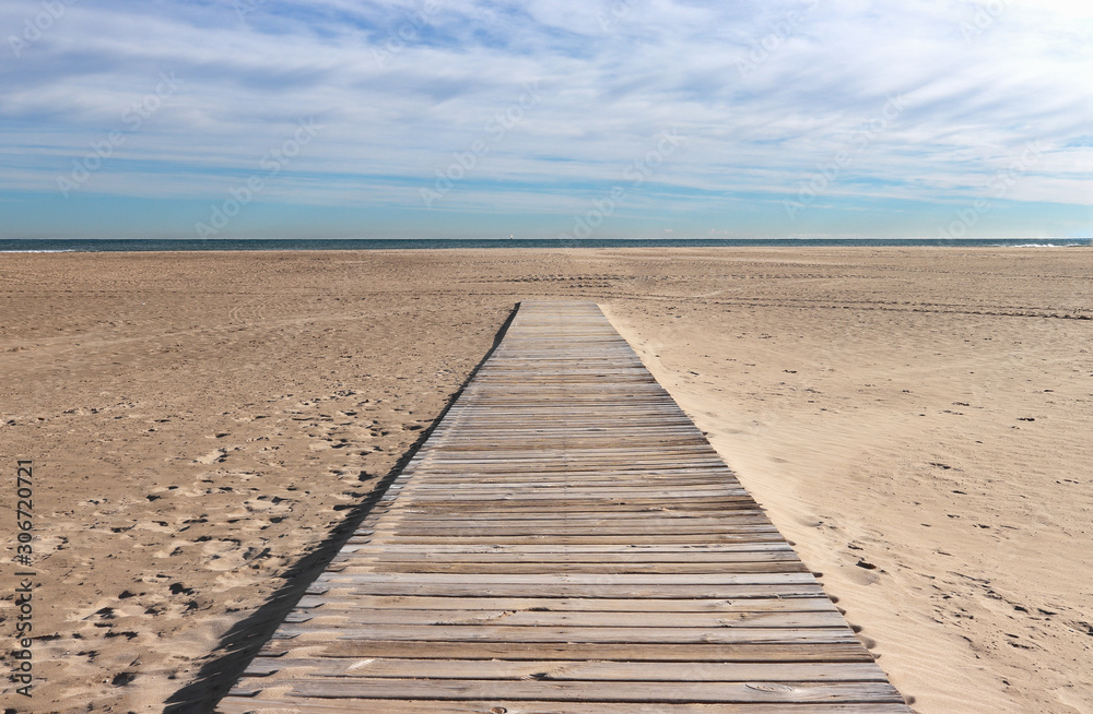 Perspective view of wooden walkway leading to the sandy beach. A blue cloudy sky and the deep blue waters of the ocean in the background. Concept for travel and tourism, beach landscape background.