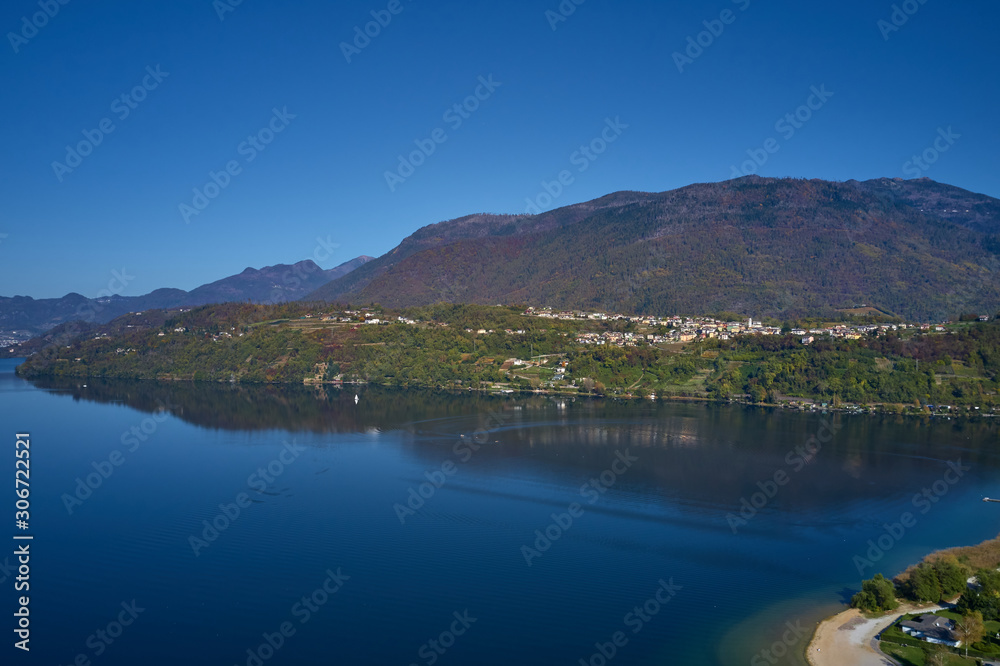 Aerial view of Lake Caldonazzo north of Italy. In the background the trees, Alps, blue sky. Reflection of mountains in water. Autumn season. Multi-colored palette of colors