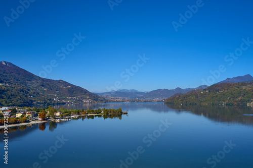 Aerial view of Lake Caldonazzo north of Italy. In the background the trees  Alps  blue sky. Reflection of mountains in water. Autumn season. Multi-colored palette of colors