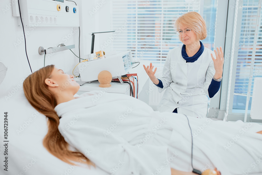 careful female doctor worry about her young patient, take care of her while she lying on bed. doctor wearing white uniform, bathrobe isolated in hospital room careful female doctor worry about her young patient, take care of her while she lying on bed. doctor wearing white uniform, bathrobe isolated in hospital room