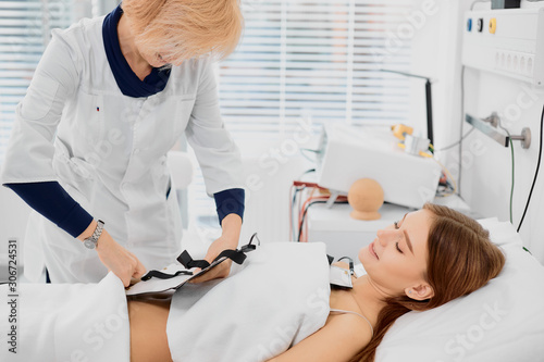 young pretty caucasian woman lying on bed and her sympathetic nurse isolated in hospital room, examining health status