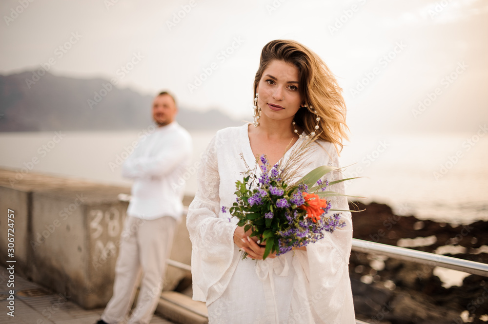 Girl with flowers in white outfit posing on seacoast Girl with flowers in white outfit posing on seacoast