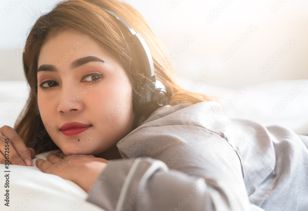 Fototapeta premium Asian women are listening to music with headphones after wake up in the morning weekend at luxury room in Relax and weekend concept in relex and entertainment concept.