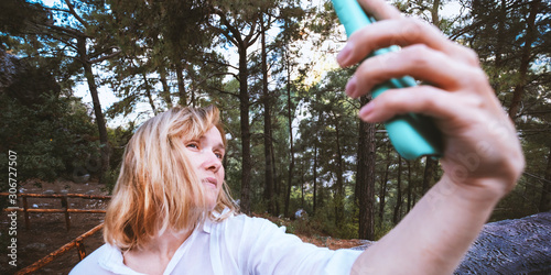 Portrait 40 years old woman with blond hair doing selfie by phone on beautiful nature background. Stock photography.