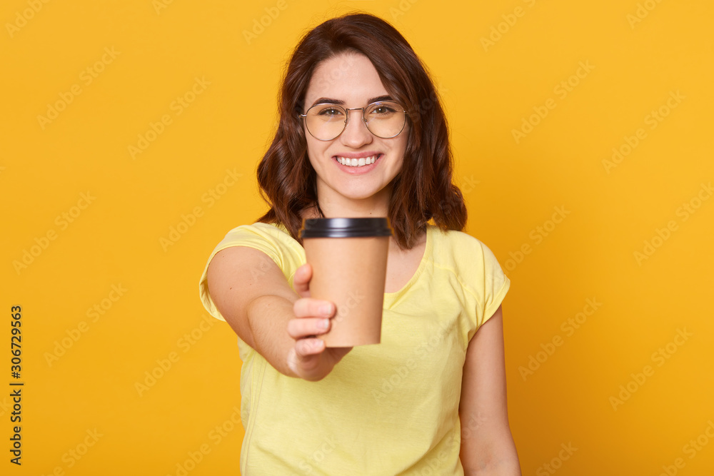 Studio shot of happy Caucasian woman holds take away cup of coffee or tea, having joyful facial expression, enjoying hot beverage, has coffee break, posing isolated over yellow studio background. Studio shot of happy Caucasian woman holds take away cup of coffee or tea, having joyful facial expression, enjoying hot beverage, has coffee break, posing isolated over yellow studio background.