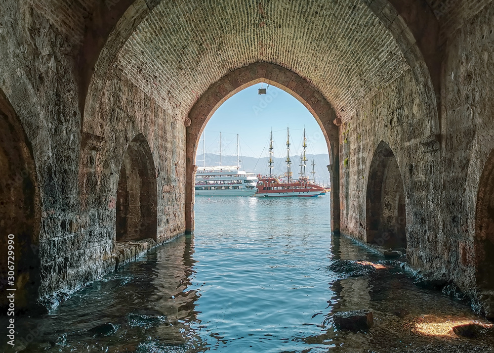 View of pleasure tourist yachts through the stone arch of an old shipyard in Turkish Alanya in the afternoon