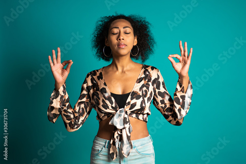  Calm african american girln relaxing, meditating. Woman calms down, breathes deeply with mudra om on blue background. photo