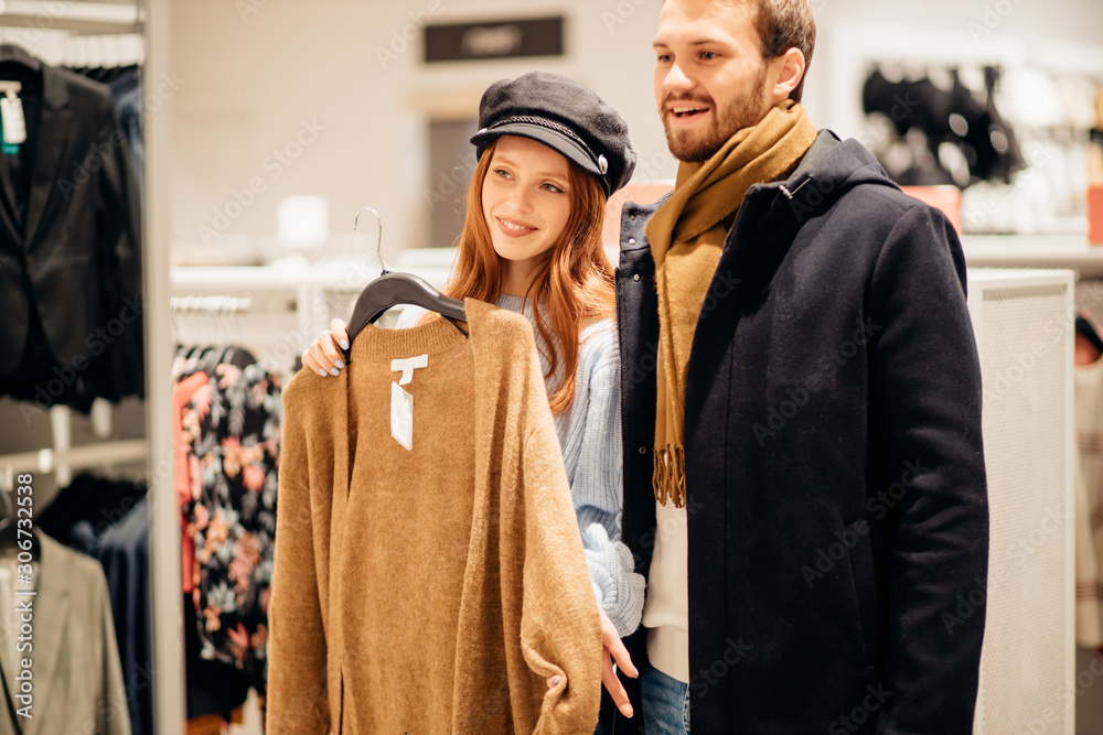 beautiful young caucasian couple watching, looking for new blouse in clothes store together with bearded caucasian husband