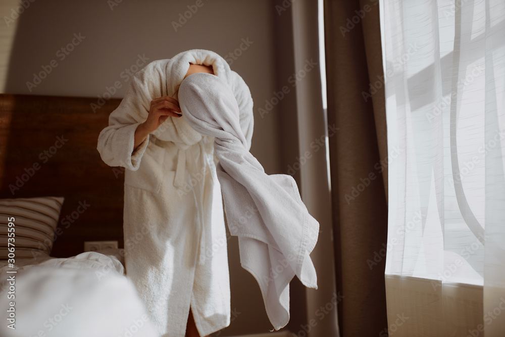 Young lady standing in bedroom after taking shower, bending forward, holding big soft towel in hands, drying hair, going to wrap wet hair in white bath towel, beauty, wellness, body care concept
