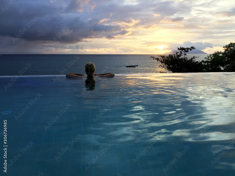Frau im Infinity-Pool blickt auf das Meer und den Horizont in der Abenddämmerung Frau im Infinity-Pool blickt auf das Meer und den Horizont in der Abenddämmerung