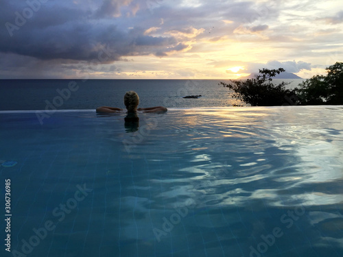 Fototapeta Naklejka Na Ścianę i Meble -  Frau im Infinity-Pool blickt auf das Meer und den Horizont in der Abenddämmerung