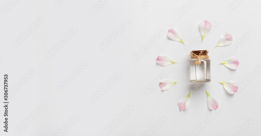 Essential oil bottle surrounded by pink petals on white Essential oil bottle surrounded by pink petals on white