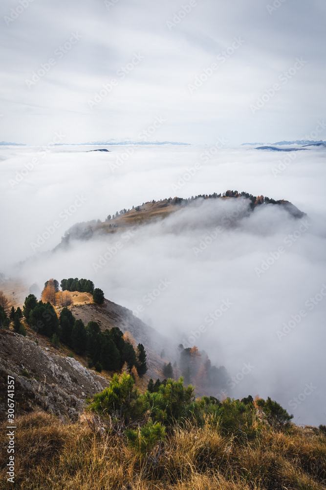 Dolomites, Italy - sunny day cloud inversion over hills with autumn colors on trees