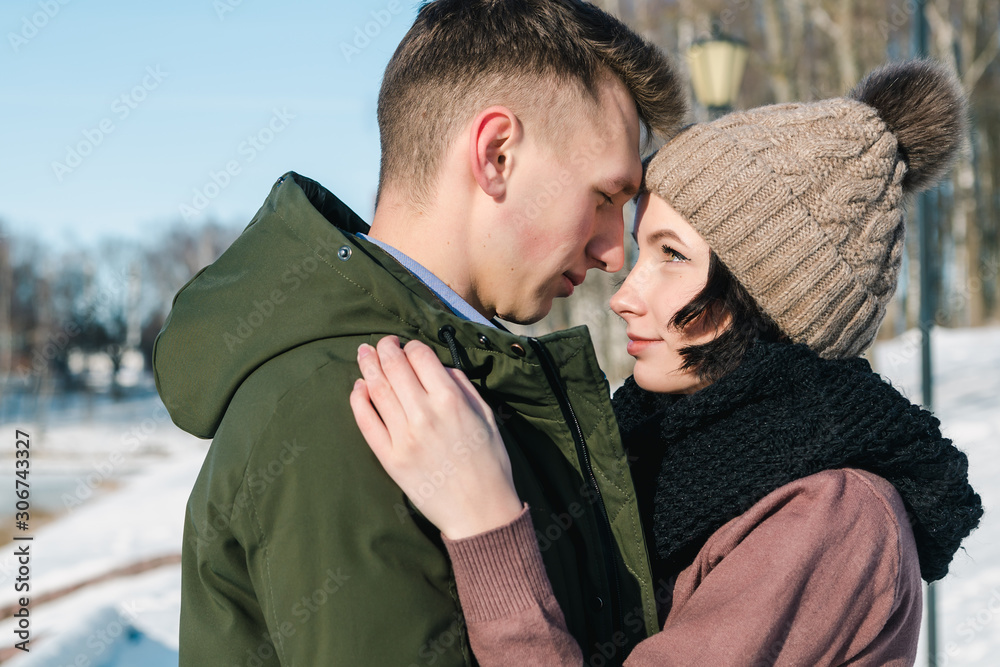 Loving young beautiful couple in the park on a bright sunny wintee day. The girl looks into the eyes of her boyfriend and smiles with tenderness Loving young beautiful couple in the park on a bright sunny wintee day. The girl looks into the eyes of her boyfriend and smiles with tenderness