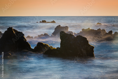 Misty water falls over lava rocks at sunrise on the Big Island in Hawaii