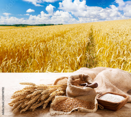 wheat ears, grains and flour on a wooden table on wheat field background