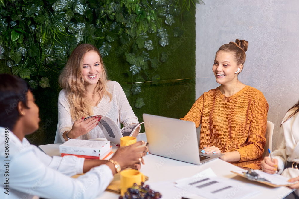 Confident young beautiful caucasian and african women hold meeting in modern green office, discussion of new business ideas and projects. business startup concept Confident young beautiful caucasian and african women hold meeting in modern green office, discussion of new business ideas and projects. business startup concept