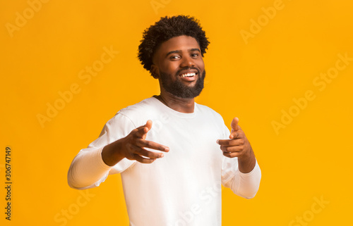 Cheerful black man greeting happily, indicating to camera