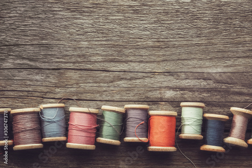 фотографія Row of vintage wooden spools of multicolored threads on wooden board