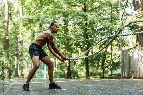 Side view of young sportsman exercising with battle ropes outdoors © Artem Varnitsin