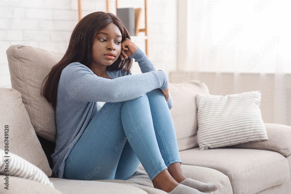 Lonely depressed african american woman sitting on couch at home