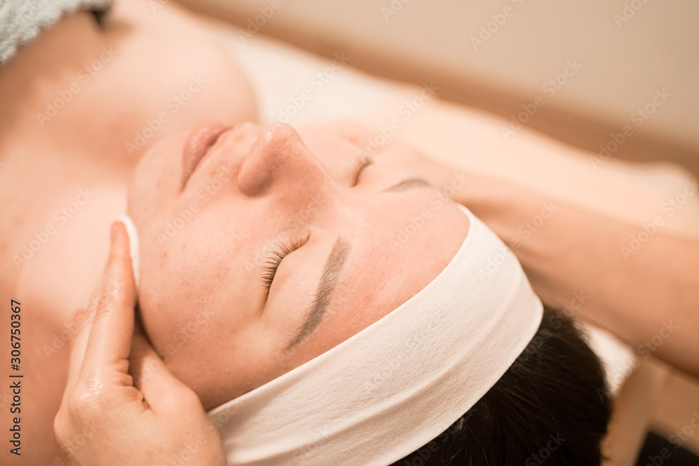 portrait of young woman washing her face with cotton pad, close up in the spa salon