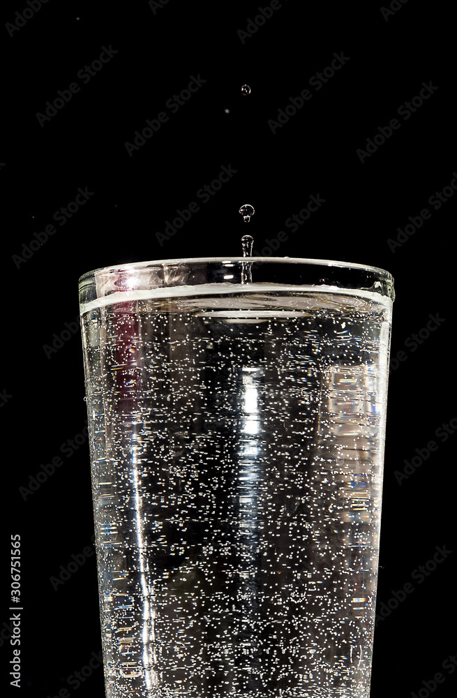 Water falling into a glass forming splashes on a black background under studio lighting Water falling into a glass forming splashes on a black background under studio lighting