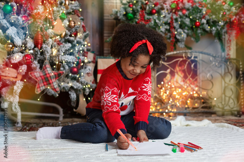 Sweet little girl writing letter to Santa in decorated living room