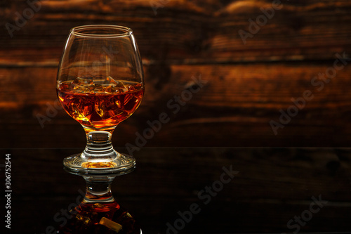 Whiskey with ice or brandy in a glass on a glass reflective surface. Whiskey with ice in a glass. Whiskey or brandy. Selective focus.