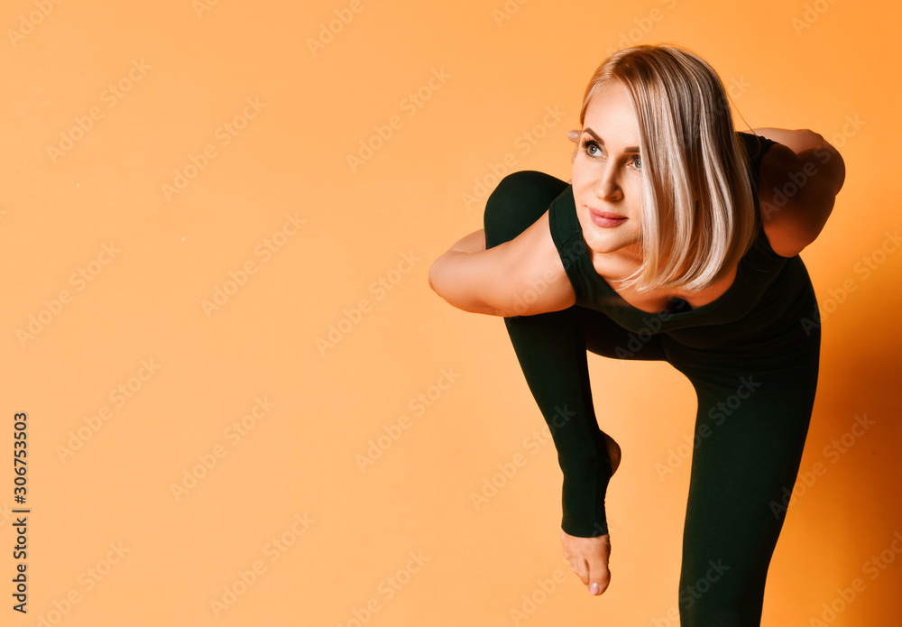 Beautiful athletic girl trainer doing yoga pose stretches in sport fitness gym club in green sportswear on yellow Beautiful athletic girl trainer doing yoga pose stretches in sport fitness gym club in green sportswear on yellow