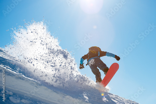 Snowboarder Riding Red Snowboard in the Mountains at Sunny Day. Big Splash of Snow. Snowboarding and Winter Sports