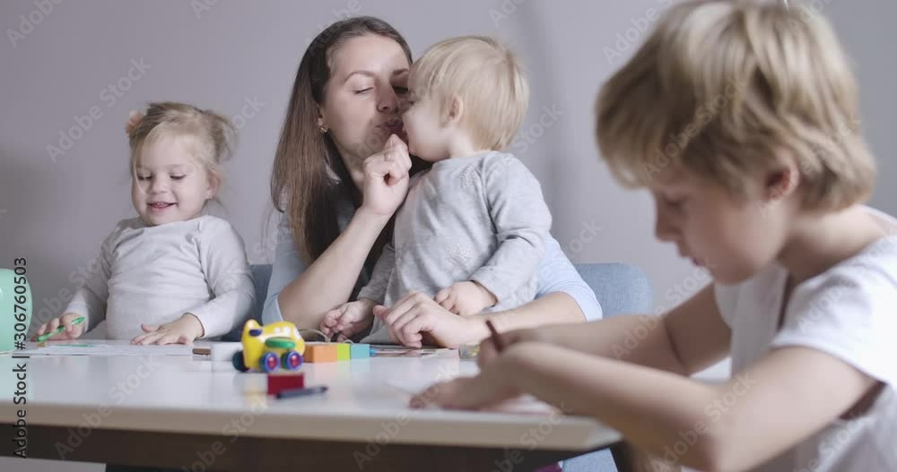 Cheerful blond baby sisters playing with mother at the background as cute schoolboy drawing on the right. Happy family spending sunny day at home. Cinema 4k ProRes HQ. Cheerful blond baby sisters playing with mother at the background as cute schoolboy drawing on the right. Happy family spending sunny day at home. Cinema 4k ProRes HQ.