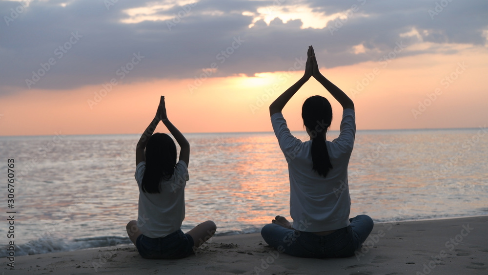Silhouette of mother and daughter doing yoga by the sea in the evening. 4k Resolution.