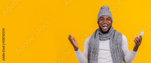 Emotional afro guy shouting and raising hands, holding phone