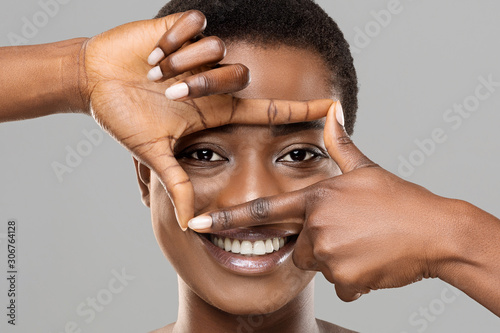 Beautiful african woman holding frame from fingers near her eyes