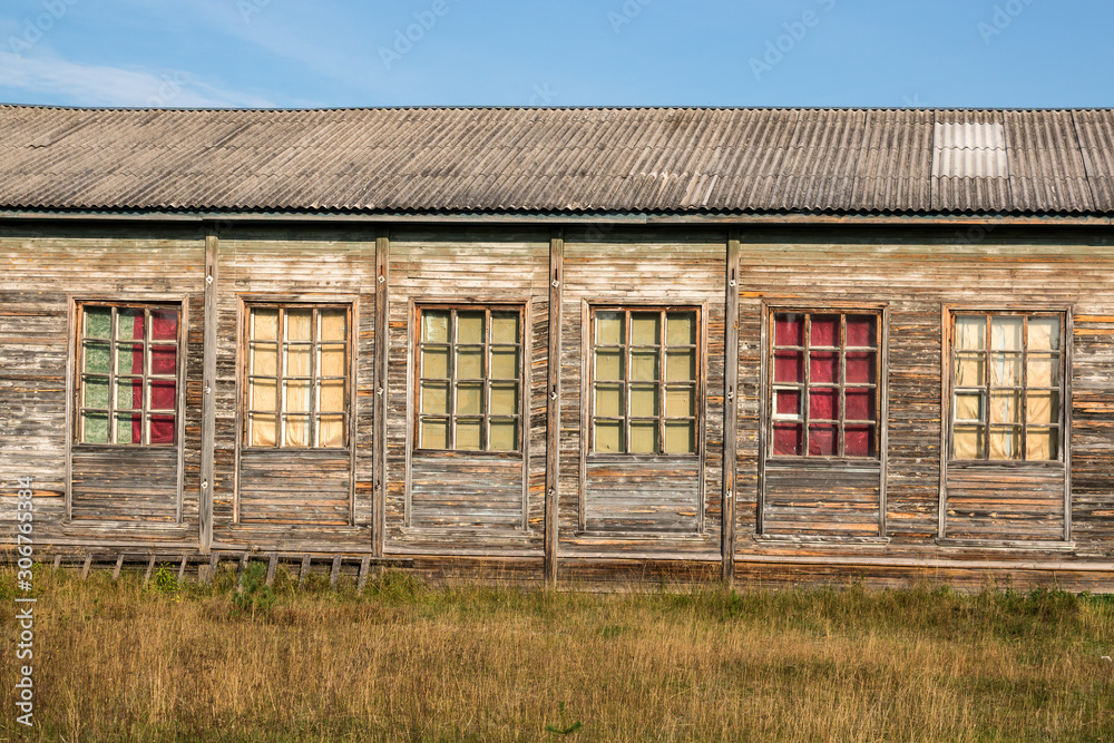 Fototapeta premium Old residential wooden houses. Windows and walls with damaged old roof with weathered paint. To close. On the street in the Arkhangelsk region of Russia.