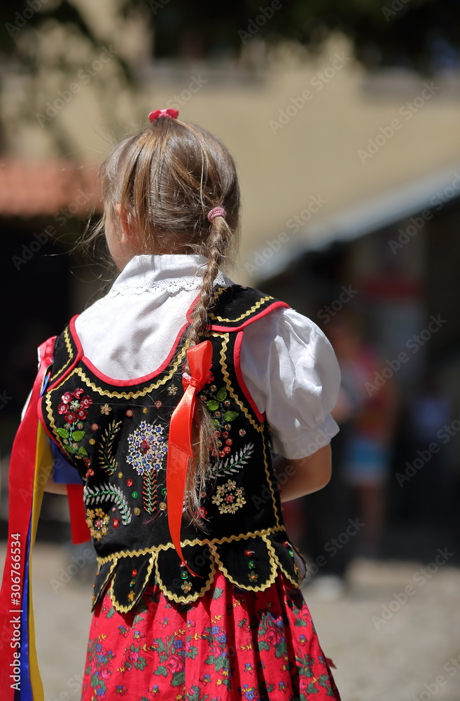 Little Polish girl in traditional folk costume stands on her back