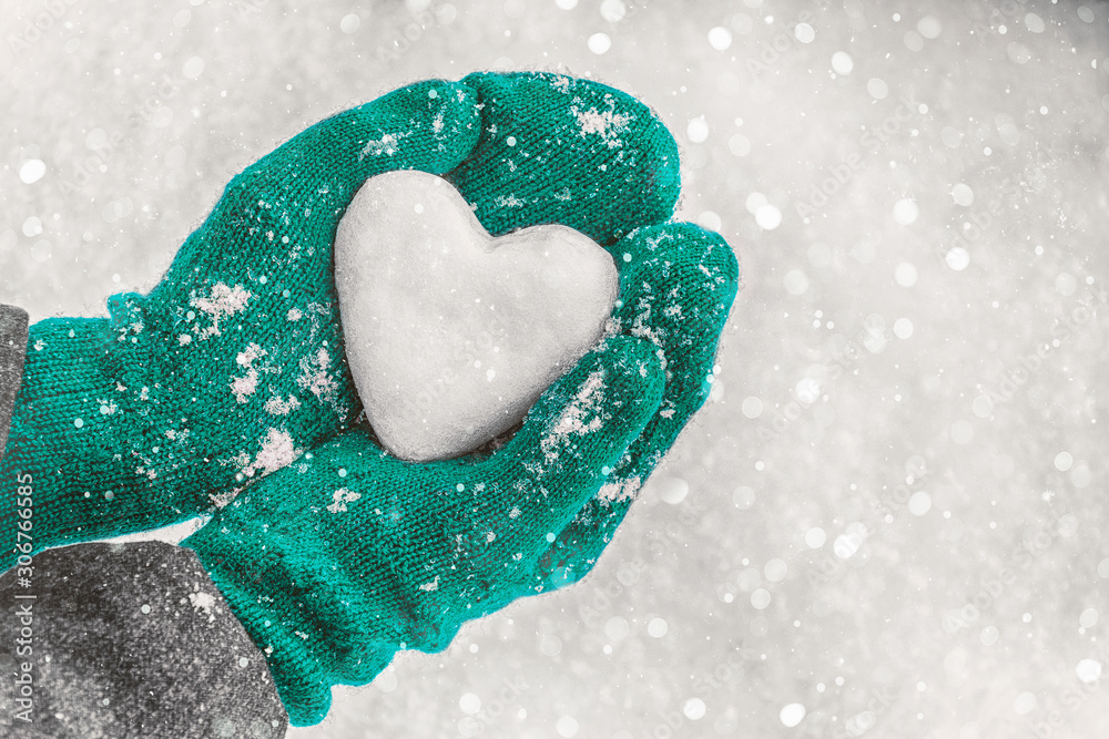Obraz premium Female hands in knitted mittens with heart of snow in winter day. Love concept. Valentine day background.