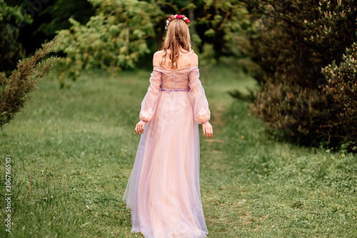 Beautiful romantic fairy girl in long dress in blooming spring garden. Gorgeous young model with perfect hairstyle in fairy forest. Fantasy art