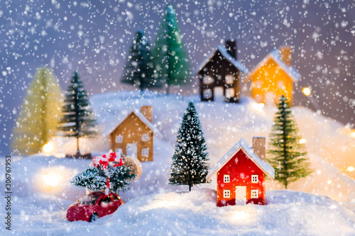 Miniature wooden houses village on the snow over blurred Christmas decoration background, toned, heavey snowfall