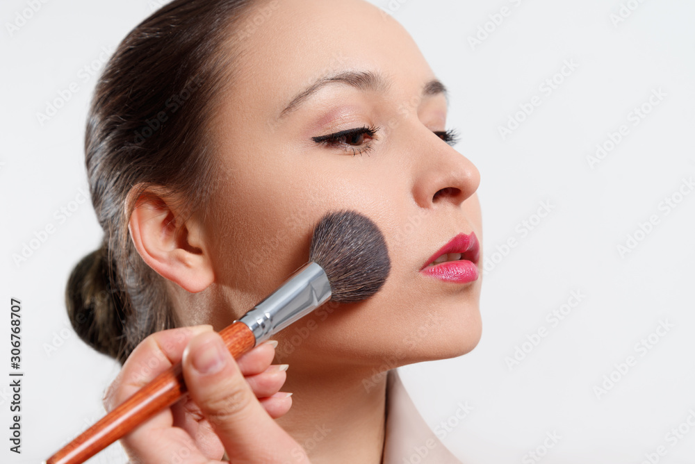 a young woman puts makeup on her face with a brush. on white background. a young woman puts makeup on her face with a brush. on white background.