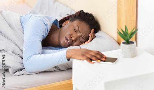 Girl Turning Off Alarm-Clock On Cellphone Lying In Bed Indoor © Prostock-studio