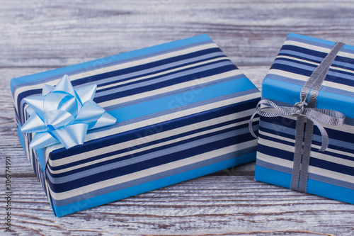 Striped gift box with blue bow. Gift boxes wrapped in blue striped paper on wooden background. Merry Christmas presents.