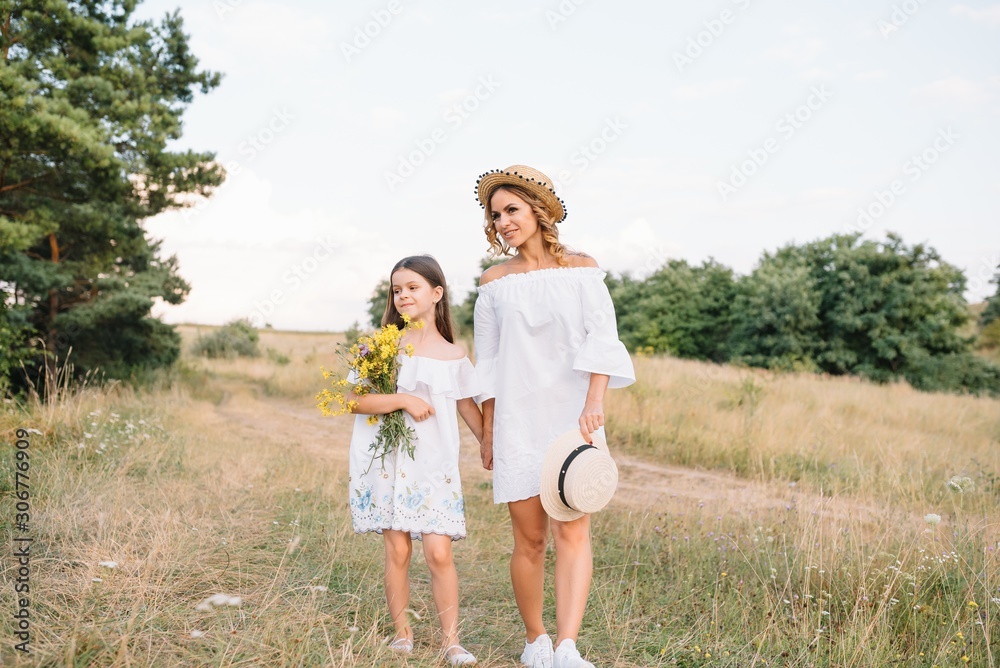 Cheerful mother and her little daughter having fun together in the summer background. Happy family in the nature background. Cute girls with colorful flowers.