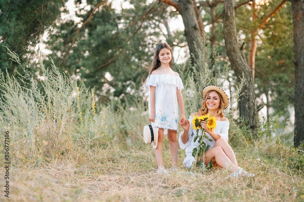 Fototapeta premium Cheerful mother and her little daughter having fun together in the summer background. Happy family in the nature background. Cute girls with colorful flowers.