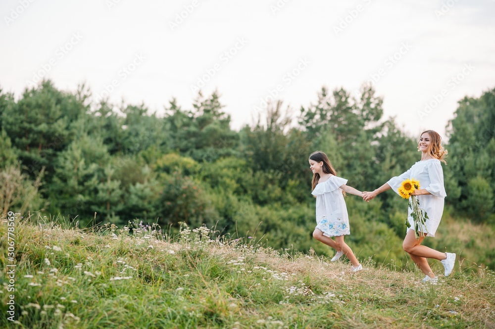Cheerful mother and her little daughter having fun together in the summer background. Happy family in the nature background. Cute girls with colorful flowers. Cheerful mother and her little daughter having fun together in the summer background. Happy family in the nature background. Cute girls with colorful flowers.