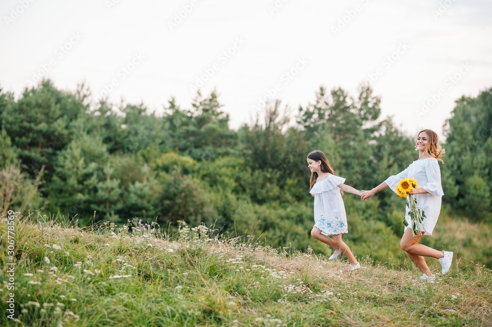 Cheerful mother and her little daughter having fun together in the summer background. Happy family in the nature background. Cute girls with colorful flowers.